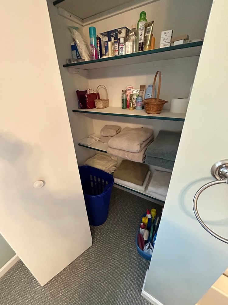 Bathroom remodel — before: linen closet with glass shelves, carpet floor, and blue laundry basket — Findlay, Ohio