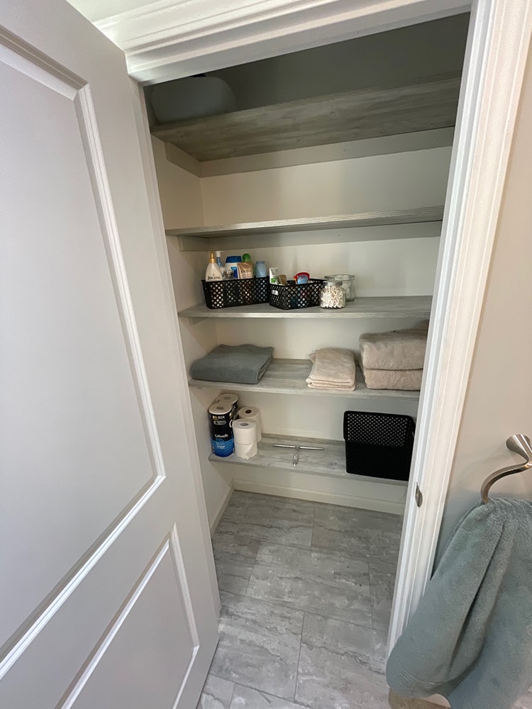 Bathroom remodel — after: updated linen closet with new shelving, crown molding, and gray tile floor — Findlay, Ohio
