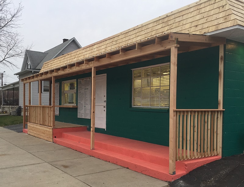 Cedar porch and overhang Findlay — during: new cedar frame, posts, and railing going up on freshly painted green building, Findlay, Ohio