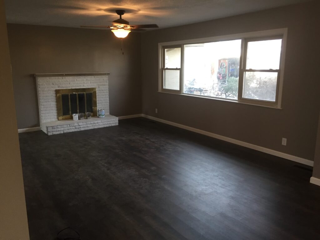 Complete home remodel Findlay — after: living room with new LVP flooring, painted brick fireplace and ceiling fan, Findlay, Ohio