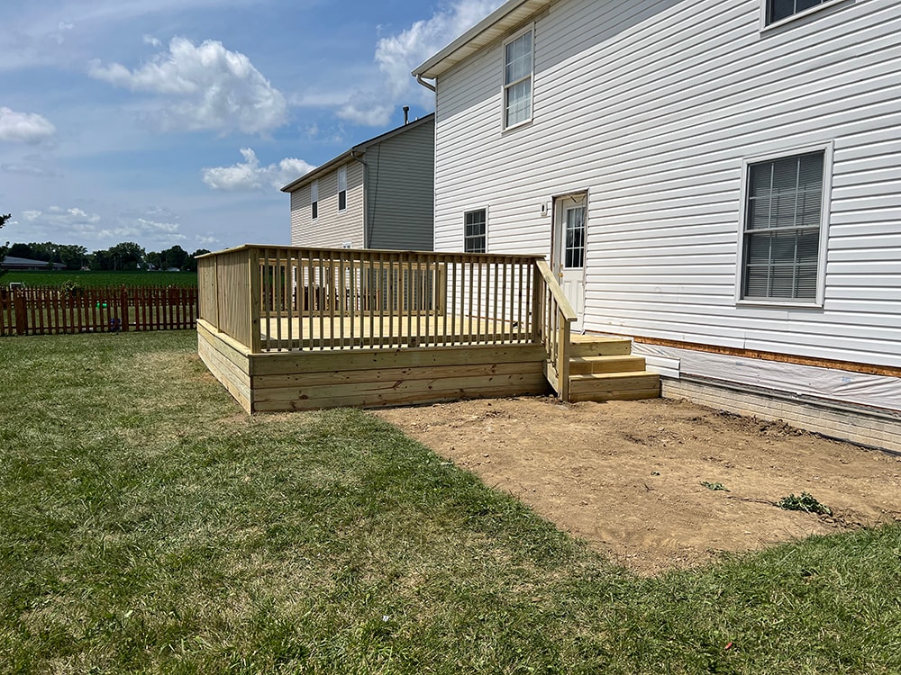 Deck addition — after: new full-width treated lumber deck with vertical spindle railing and side stairs, angled view from yard, Findlay, Ohio
