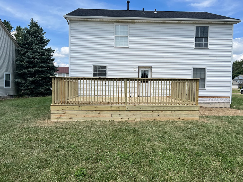 Deck addition — after: new treated lumber deck with railing, straight rear view showing full width of deck against two-story home, Findlay, Ohio