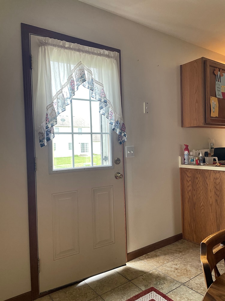 Deck addition — interior before: original solid entry door with window and curtains leading to backyard, kitchen view, Findlay, Ohio