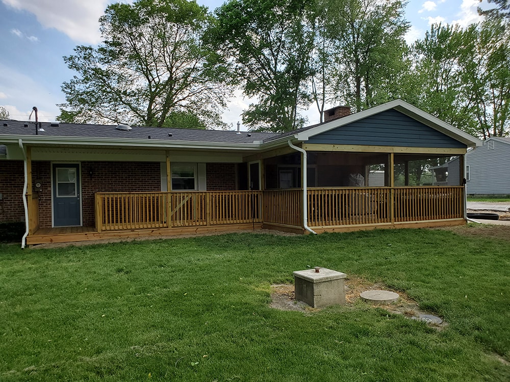 Deck addition Findlay — after: wide yard view of completed full deck and screened room with blue gable siding, treated railing, and green lawn, Findlay, Ohio