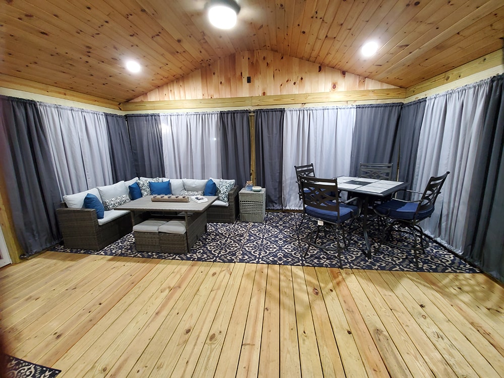 Deck addition Findlay — after: interior at night with privacy curtains closed, recessed lighting, knotty pine vaulted ceiling, sectional sofa, and dining set on blue rug, Findlay, Ohio