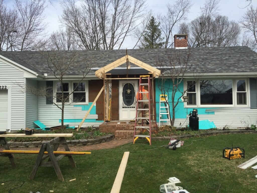 Front porch roof addition Findlay — during: gable framing standing with house wrap exposed and tools in yard, Findlay, Ohio