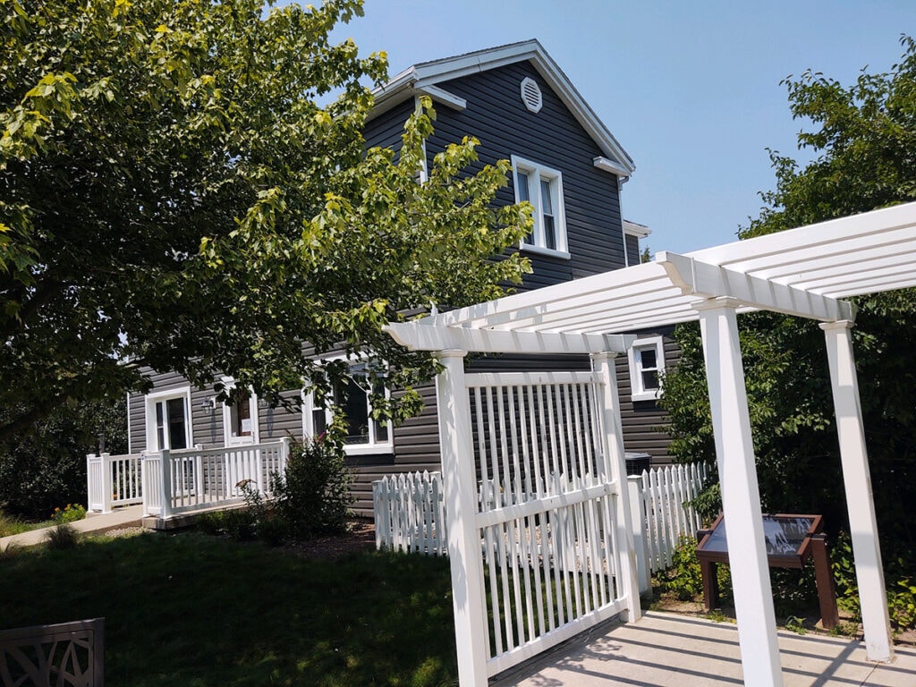 Hancock Park District siding — after: front entry of Welcome Center with new dark charcoal vinyl siding, white railing, and pergola, Findlay, Ohio