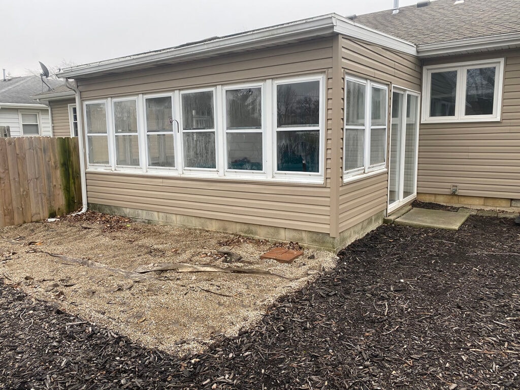 Large room addition Findlay — before: original sunroom exterior close-up showing full bank of windows and concrete block foundation, Findlay, Ohio