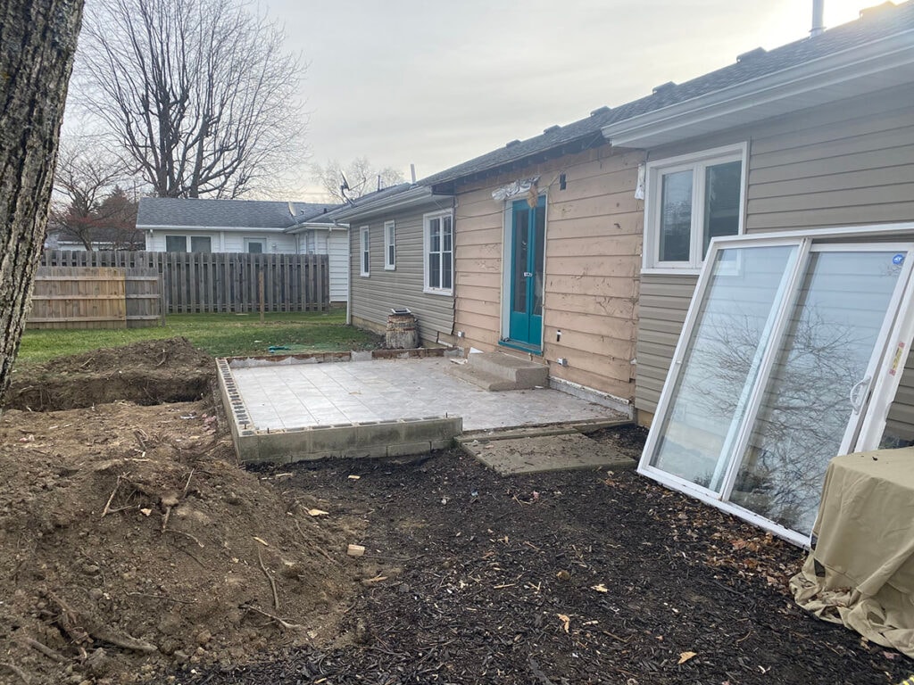 Large room addition Findlay — demo stage: old sunroom removed, new concrete slab poured, windows staged on ground ready for installation, Findlay, Ohio
