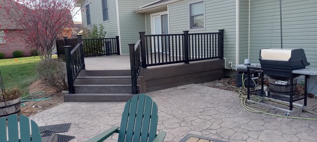 New composite deck — after: completed deck with black railing, Adirondack chairs, and stamped concrete patio — Findlay, Ohio