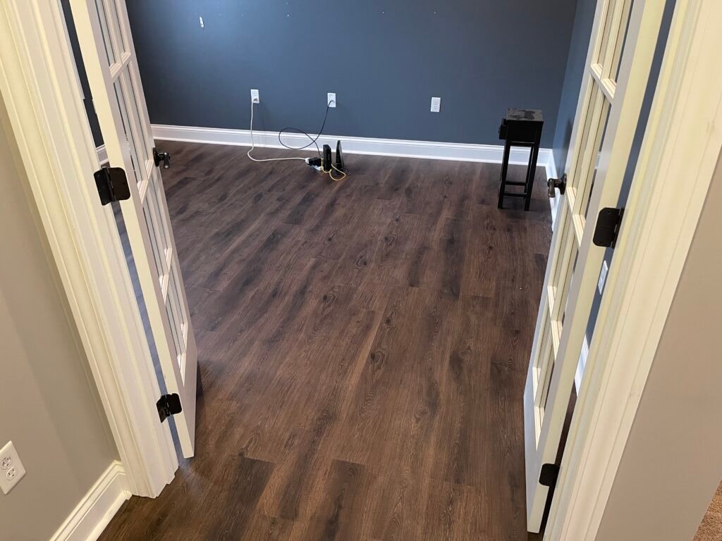 New LVP flooring — bedroom with dark wood-look LVP and blue accent wall viewed through double doors, Findlay, Ohio