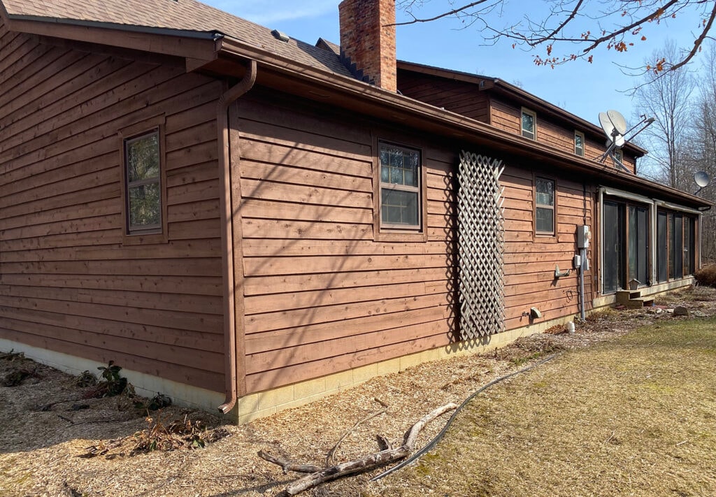 New siding Findlay — before: side of home with original brown cedar siding, lattice trellis, and sunroom windows, Findlay, Ohio