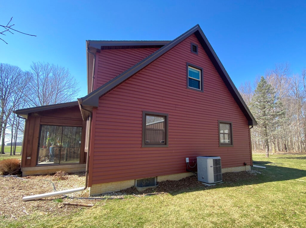 New siding Findlay — after: wide angle of garage end and sunroom with new dark red vinyl siding and AC unit, Findlay, Ohio