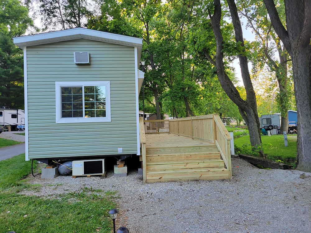 New treated deck — after: green park model with completed treated wood deck and railing — Wapakoneta campground