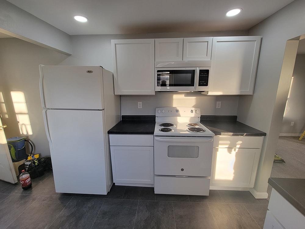 Rental home remodel after — kitchen with new white cabinets, countertops, appliances, and tile flooring, Findlay, Ohio