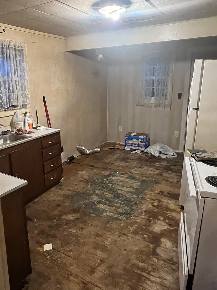 Rental home remodel before — kitchen with dark cabinets, old stove, and heavily damaged flooring, Findlay, Ohio