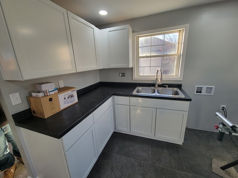 Rental home remodel after — kitchen with white shaker cabinets, black countertops, stainless sink, and dark tile flooring, Findlay, Ohio