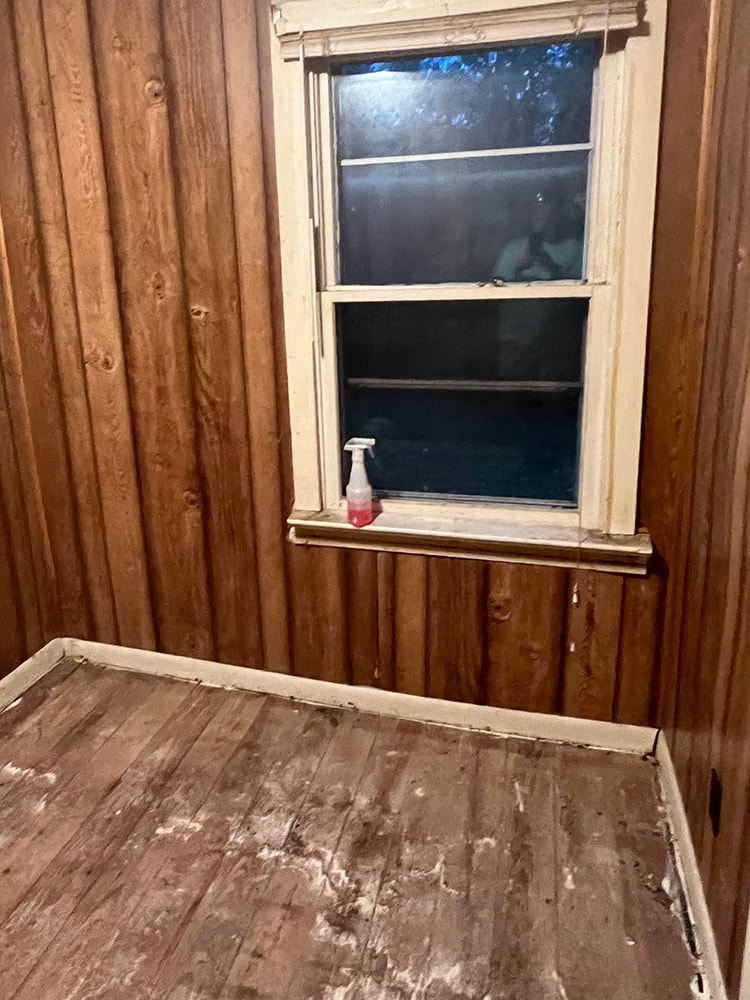 Rental home remodel before — small room with wood paneling, old window, and worn wood flooring, Findlay, Ohio