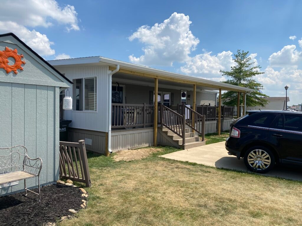 Roof addition existing deck Findlay — after: exterior wide shot of completed home with full flat roof over deck, white beadboard soffit, treated wood posts, new siding on wall section, and black SUV in driveway, Findlay, Ohio