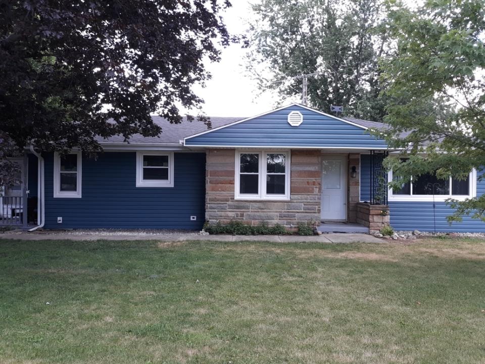Siding job Findlay — after: completed front of home with bold blue vinyl siding, stacked stone accent, white trim, white entry door, and green lawn, Findlay, Ohio