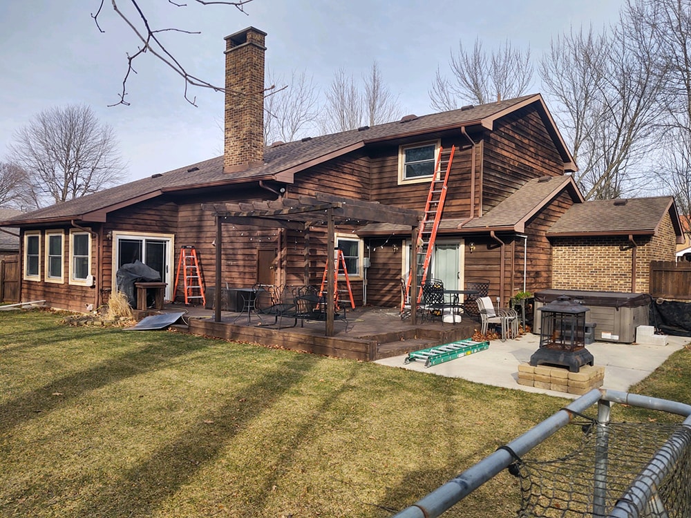 Siding job with brick — before: rear view of home with original dark wood siding and ladders staged for work, Findlay, Ohio