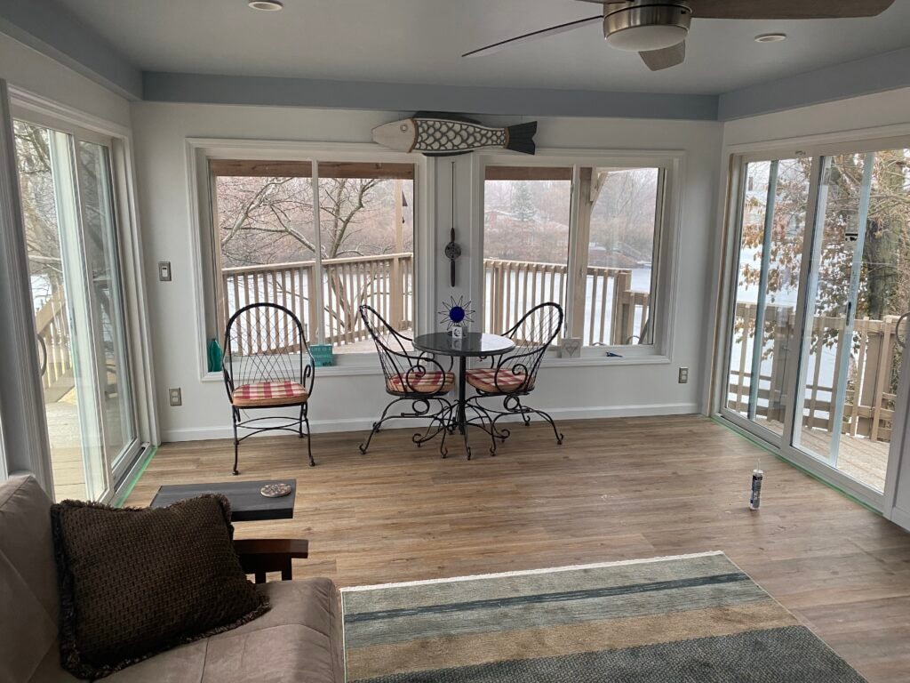 Sunroom transformation Fostoria — after: interior of finished four-season room with LVP flooring, ceiling fan, dining set, sliding glass doors on three sides, and water views, Fostoria, Ohio