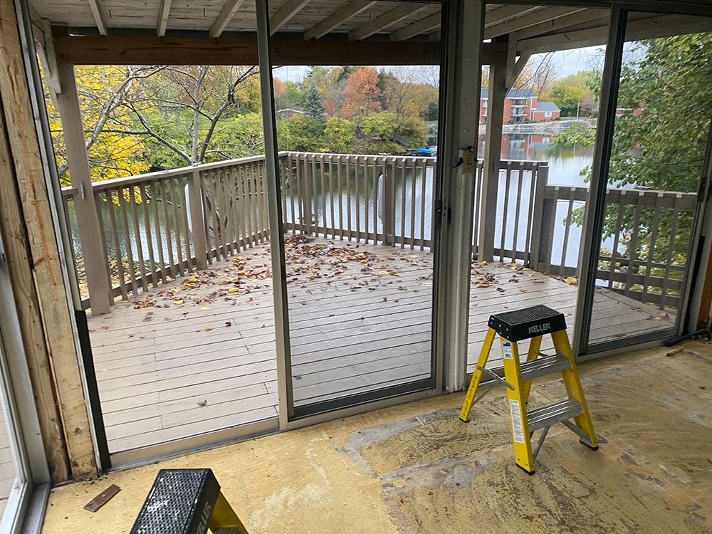 Sunroom transformation Fostoria — before: interior of original sunroom looking out through sliding glass doors to deck and water view, Fostoria, Ohio