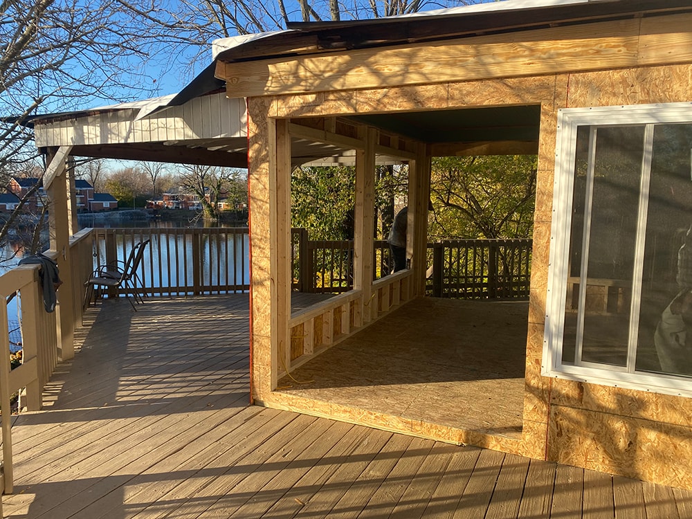 Sunroom transformation Fostoria — framing stage: new OSB sheathed walls and floor from deck angle, water view in background at golden hour, Fostoria, Ohio