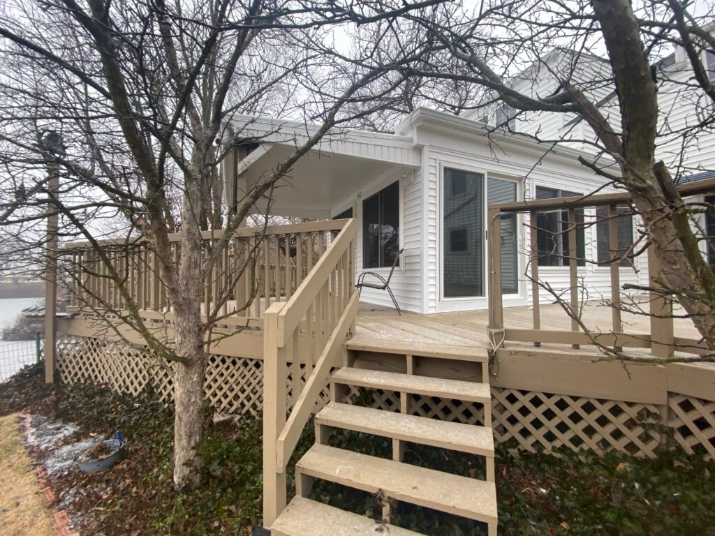 Sunroom transformation Fostoria — after: exterior from yard showing completed addition with new white vinyl siding, sliding glass door, and deck stairs in winter, Fostoria, Ohio
