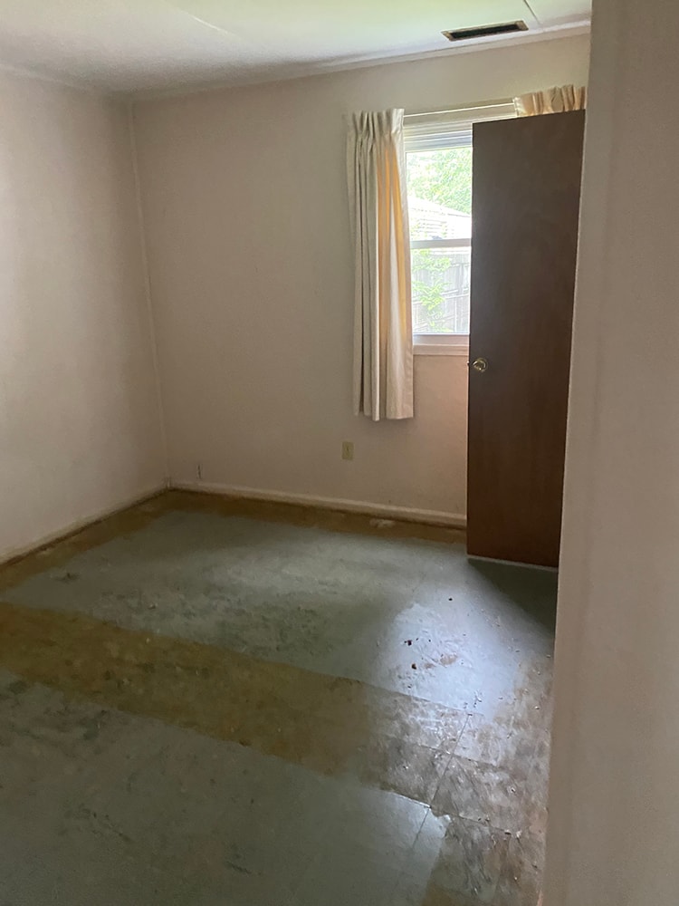 Whole house remodel before — bedroom with bare concrete subfloor, old curtains, and worn walls, Fostoria, Ohio
